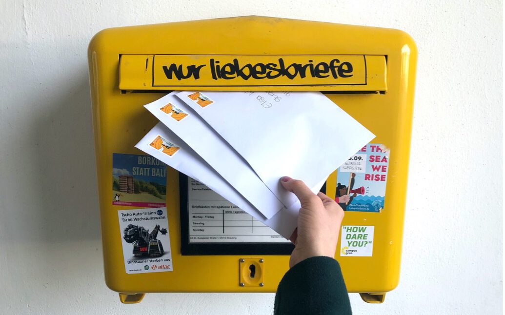 Briefkasten mit einer Hand, die die Briefe mit den FFP2 Masken in den Briefkasten wirft.